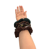 Hand wearing three brown scrunchies on a white background