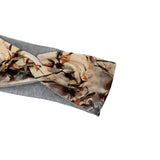A gray fabric headband featuring a large twisted front panel with an abstract watercolor-style print in beige, brown, and orange tones, shown on a plain white background.