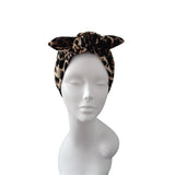 A leopard print fabric headband with a large twisted knot, displayed on a white mannequin head against a plain white background.