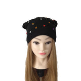 A black beanie hat with small multicolored rhinestone embellishments, displayed on a mannequin head with long light brown hair against a plain white background.