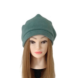 A dark teal-green knit beanie hat displayed on a mannequin head with long light brown hair against a plain white background.