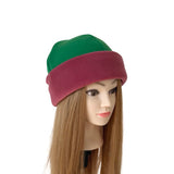 A two-tone fleece beanie hat with a green top and a burgundy folded brim, displayed on a mannequin head with long light brown hair against a plain white background.
