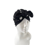 Black headband with decorative bow on a mannequin head against a white background