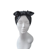 A black satin-like headband with a large bow, displayed on a white mannequin head and shoulders against a plain white background.