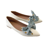 White flats with green floral bow accents on a white background