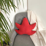 Red leaf-shaped pillow on a gray chair with a plant in the background