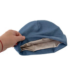 Hand holding a blue fabric item with beige interior on a white background