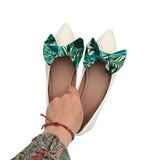 White pointed-toe shoes with green leaf-patterned bows on a white background