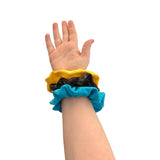 Hand wearing a blue scrunchie with a yellow top on a white background