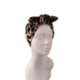 A leopard print fabric headband with a large bow, displayed on a white mannequin head against a plain white background.