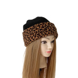 A leopard print and black beanie hat displayed on a mannequin head with long light brown hair against a plain white background.
