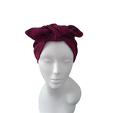 A deep burgundy ribbed fabric headwrap turban with a large bow, displayed on a white mannequin head against a plain white background.