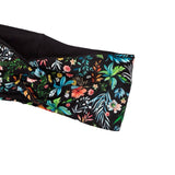 A close-up of a black fabric headband featuring a vibrant, multicolored tropical floral and leaf print, shown against a plain white background.