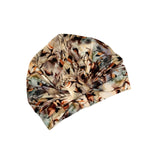A soft fabric turban cap with an abstract watercolor-style print in beige, brown, black, and muted green, shown on a plain white background.