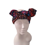 A multicolor floral headwrap turban hat with a large bow on top, displayed on a light gray mannequin head against a white background.