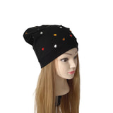 A black slouchy beanie hat with small colorful rhinestone studs, displayed on a mannequin head with long blonde hair against a plain white background.