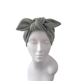 A ribbed fabric turban-style headwrap in a muted sage green color, styled on a white mannequin head against a plain white background.