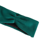 A close-up of a dark teal green twisted fabric headband with a black inner lining, shown on a plain white background.
