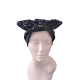 A dark navy blue patterned headwrap turban hat with a bow, displayed on a light pink mannequin head against a white background.