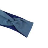 A close-up of a knotted fabric headband in dusty blue with a dark navy inner lining, shown on a plain white background.
