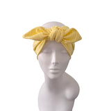 A yellow fabric headwrap with a large bow, displayed on a white mannequin head against a plain white background.