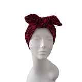 A red and black zebra-print fabric headwrap styled in a large bow on a white mannequin head against a plain white background.