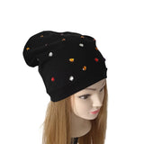 A black slouchy beanie hat with small scattered rhinestone embellishments in red, gold, and silver, displayed on a mannequin head with long light brown hair against a plain white background.