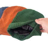 Green knitted beanie held by a hand with orange and blue beanies in the background.