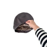 Gray beanie being held by a hand with a striped sleeve on a white background