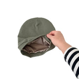 Green beanie being held by a hand with striped sleeves on a white background