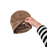 Brown ribbed knit beanie held by a hand with a striped sleeve on a white background
