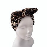 A leopard print knotted headband displayed on a white mannequin head against a plain white background.