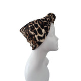 A leopard print headwrap or turban hat displayed on a white mannequin head in profile against a plain white background.