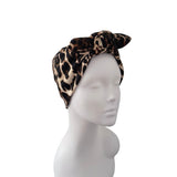 A leopard print fabric hair bow headband displayed on a white mannequin head against a plain white background.