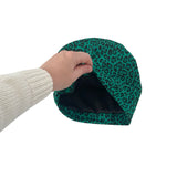 Green leopard print pet bed being held by a person wearing a beige sweater.