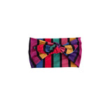 A colorful striped bow headband with vertical stripes in pink, purple, yellow, teal, and black, centered on a plain white background.