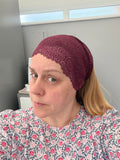 Person wearing a maroon headscarf with a pattern, sitting indoors.