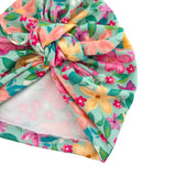 A knotted fabric headband or turban hat with a pastel floral print on a mint green background, featuring pink, yellow, and peach flowers with green leaves. The underside shows a light pink lining.