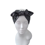 A black satin bow headband displayed on a white mannequin head against a plain white background.