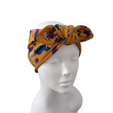 A mustard yellow fabric headwrap with a purple and blue abstract pattern, styled on a white mannequin head against a plain white background.