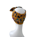 A mustard yellow crinkled fabric headband with a multicolor abstract print, displayed on a white mannequin head against a white background.