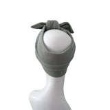 A ribbed knit headband in a muted sage green color, styled on a white mannequin head with a bow at the top, set against a plain white background.
