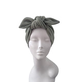 An olive green ribbed fabric headwrap turban with a large bow, displayed on a white mannequin head against a plain white background.