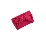 A bright pink textured fabric headband with a large twisted knot in the center, displayed on a clean white background.