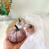 Decorative pumpkins in pink, silver, and gold on a white surface with a blurred background.