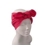 A bright pink textured fabric headband with a large bow, displayed on a white mannequin head against a plain white background.