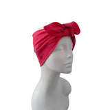 A bright red textured fabric headwrap turban with a large bow, displayed on a white mannequin head against a plain white background.