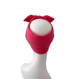 A bright pink knit headband with a large bow on top, displayed on a white mannequin head against a plain white background.
