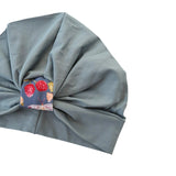 Gray fabric turban with a colorful patterned tag on a white background