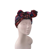 A multicolor floral headwrap turban hat with two side bows, displayed on a light gray mannequin head against a white background.
